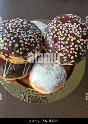 Pfannkuchen mit Schokoladenglasur und Streuseln und mit Puderzucker, bekannt als Donuts für Karneval Stockfoto