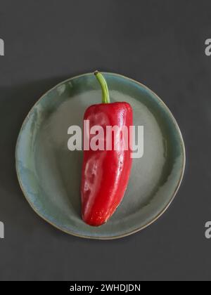 Eine rote Paprika mit grünem Stiel liegt auf einer grünen Platte Stockfoto