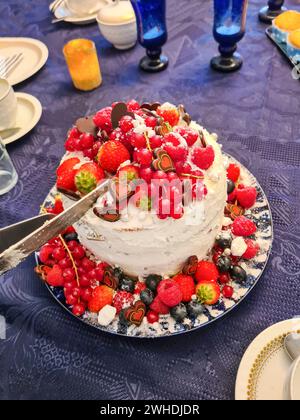 Auf einer blauen Tischdecke steht ein festlicher Sahnekuchen mit Früchten wie Erdbeeren, Himbeeren, Johannisbeeren und Heidelbeeren als Dekoration Stockfoto