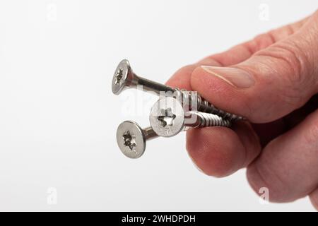 Die Hand des Mannes hält drei Torx-Holzschrauben aus Edelstahl, weißer Hintergrund, Stockfoto