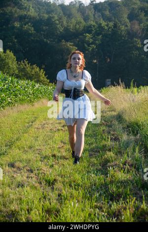 Eine hübsche junge Frau, die ein weißes, kurzes Kleid trägt, in grüner Natur vorwärts rennt Stockfoto