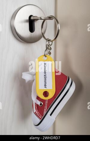 Schlüssel mit gelbem Schlüsselanhänger und Miniatur-Sneaker im Türschloss, Aufschrift ëKinderzimmerë, Detail, Stockfoto