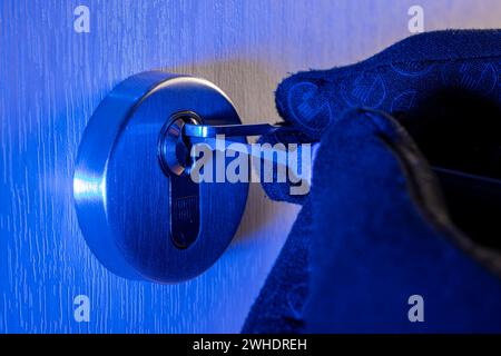 Einbrecher öffnet Zylinderschloss mit Schloßwerkzeug, Männerhand mit Handschuh, Detail, blaues Licht, symbolisches Bild, Hauseinbruch, Stockfoto