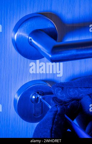 Einbrecher öffnet Zylinderschloss mit Schloßwerkzeug, Männerhand mit Handschuh, Detail, blaues Licht, symbolisches Bild, Hauseinbruch, Stockfoto