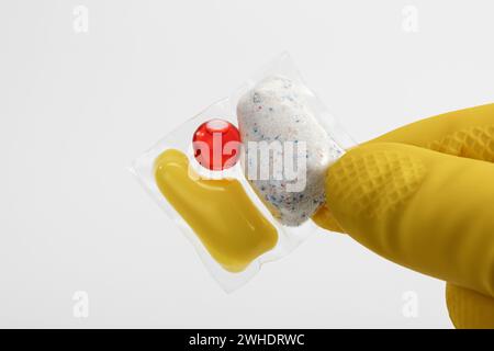 Handgriff Geschirrspüler aus wasserlöslicher Folie, gelber Schutzhandschuh, weißer Hintergrund, Stockfoto