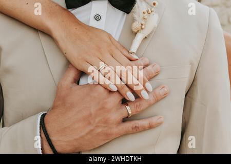 Braut umarmt Bräutigam, hält Hände, Eheringe, Hand auf Herz Stockfoto