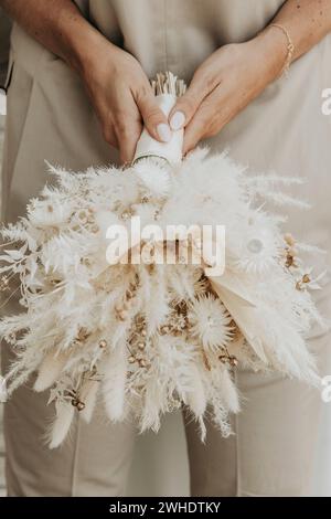 Die Braut umarmt den Bräutigam mit einem Blumenstrauß aus getrockneten Blumen Stockfoto