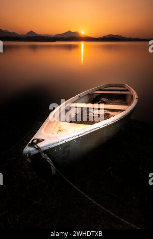 Grün-weißes Ruderboot auf dem Hopfensee mit einem goldgelben Sonnenuntergang über dem Alpenpanorama im Hintergrund Stockfoto