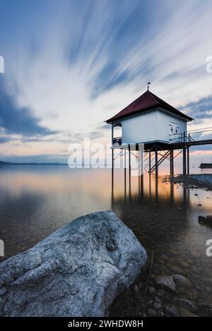 Abendliche Atmosphäre am Seeufer mit Wolken. Badehaus mit Steg und großem Felsen, sogenannte Roßtränke bei Wasserburg am Bodensee, Landkreis Lindau, Bayern, Süddeutschland, Deutschland Stockfoto