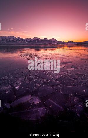 Sonnenuntergang über dem gefrorenen Hopfensee mit Eisschilden im Vordergrund und Bergen im Hintergrund, Hopfen am See, Ostallgäu, Allgäu, Schwaben, Bayern, Süddeutschland, Deutschland Stockfoto