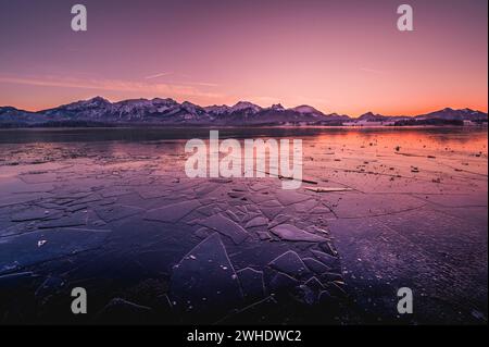 Sonnenuntergang über dem gefrorenen Hopfensee mit Eisschilden im Vordergrund und Bergen im Hintergrund, Hopfen am See, Ostallgäu, Allgäu, Schwaben, Bayern, Süddeutschland, Deutschland Stockfoto