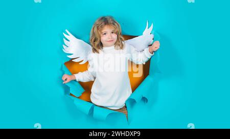 Valentinstag. Lächelnder Engel, der durch das Papierloch schaut. Kleiner Cupid Junge in weißen Flügeln. Süßes Kind in Engelsflügeln. Valentinstag Stockfoto