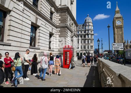 Touristen stehen an, um ein Foto mit der berühmten roten K2-Telefonbox zu machen, mit Big Ben im Hintergrund Parliament Square, London, Großbritannien. August 2023 Stockfoto