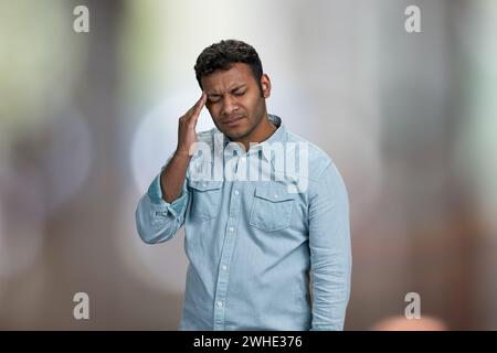 Junger asiatischer Mann, der an Kopfschmerzen leidet. Abstrakter Bokeh-Hintergrund. Gesundheitskonzept. Stockfoto