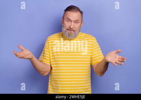 Foto eines gleichgültigen verwirrten älteren Mannes mit weißem Bart gekleidetem gestreiftem T-Shirt, das Schultern zuckt, isoliert auf lila Hintergrund Stockfoto