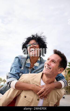 Reife multirassische freudige Touristenliebe Paar Huckepack steht im Freien und genießt einen glücklichen Urlaub. Stockfoto