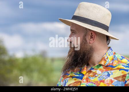 Junger bärtiger Mann mit Fedorahut, der glücklich lächelt. Nahporträt eines bärtigen jungen Mannes, der legere Kleidung trägt und mit einem in die Kamera schaut Stockfoto