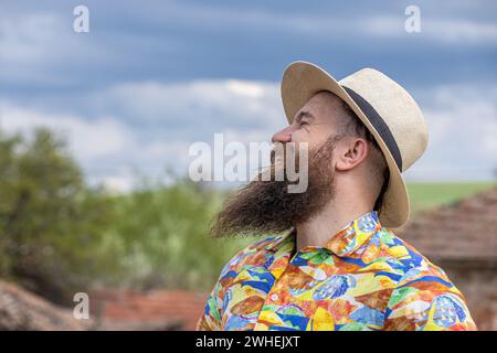 Junger bärtiger Mann mit Fedorahut, der glücklich lächelt. Nahporträt eines bärtigen jungen Mannes, der legere Kleidung trägt und mit einem in die Kamera schaut Stockfoto