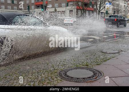 '21.12.2023, Deutschland, Berlin, Berlin - Auto fährt auf einer Straße durch eine große Pfütze. 00S231221D266CAROEX.JPG [MODELLVERSION: NEIN, EIGENSCHAFTSFREIGABE: NEIN Stockfoto