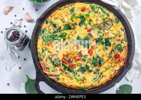 Brunch Eierfrittata mit Spinat, gebratenen roten Paprika, Pilzen, Käse und Kräutern, in gusseiserner Pfanne, horizontal, Blick von oben Stockfoto