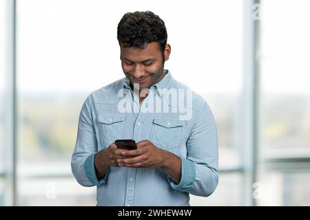 Junger lächelnder Mann, der eine Nachricht auf seinem Handy schreibt. Mensch, Technologie und Internet-Kommunikationskonzept. Stockfoto