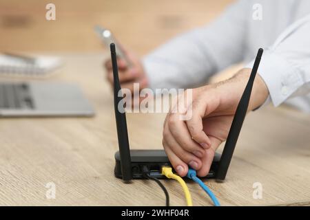 Mann, der Kabel in den WLAN-Router an einem Holztisch drinnen steckt, Nahaufnahme Stockfoto