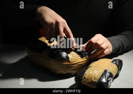 Schmuggel und Drogenhandel. Mann, der ein Paket mit Betäubungsmitteln öffnet, mit einem Koffer in der Dunkelheit, Nahaufnahme Stockfoto