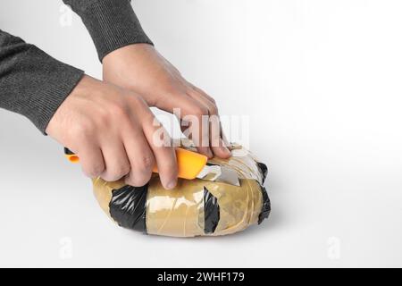 Schmuggel und Drogenhandel. Mann, der ein Paket mit Betäubungsmitteln mit einem Koffer auf weißem Hintergrund öffnet, Großaufnahme Stockfoto