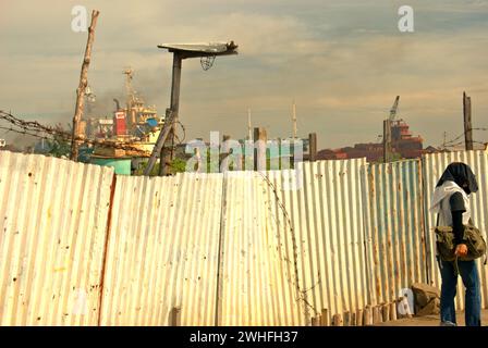 Ein Zaun, der eine schmale Straße mit einem Schiffsbrecher trennt, in der Nähe des Küstendorfes Marunda in Cilincing, Jakarta, Indonesien. Stockfoto