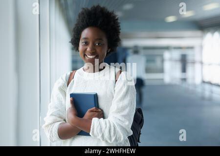 Afrikanisches Mädchen, Porträt und Flur des Colleges mit einem Lächeln aus dem Glück der Ausbildung in der Akademie. Schüler, Lerner und Notizbuch zur Hand mit Stockfoto