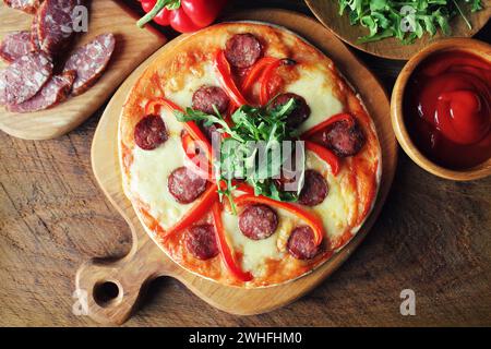 Hot hausgemachte Pizza mit Salami, paprica, Rucola auf hölzernen Tisch. Ansicht von oben Stockfoto