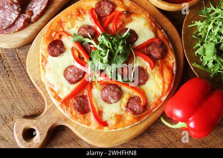 Hot hausgemachte Pizza mit Salami, paprica, Rucola auf hölzernen Tisch. Ansicht von oben Stockfoto