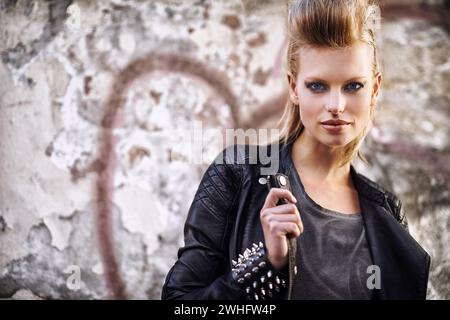 Frau, Porträt und selbstbewusst in angesagter Mode mit Punkrock-Frisur, Biker und cool in flippiger Kleidung an der Graffiti-Wand. Junges Modell, Gesicht und Stockfoto