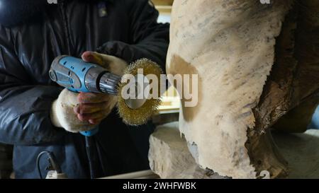 Holzarbeiter mit einem Schleifgerät in den Händen neben einem Stück Naturholz, mit einer runden Metallbürste, um die Oberfläche eines Holzmaterials zu behandeln Stockfoto