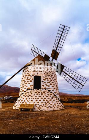 Eine traditionelle Windmühle steht majestätisch vor dem Hintergrund des bewölkten Himmels und der trockenen Landschaft in Fuerteventura, Spanien. Stockfoto