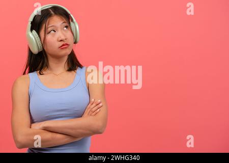 Junge nachdenkliche Chinesin isoliert auf rosafarbenem Hintergrund, Musik zu hören. Stockfoto