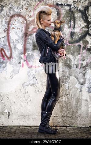 Frau, Liebe und Hund in trendiger Mode mit Punkrock-Frisur, funky und mit chihuahua durch Graffiti-Wand verbunden. London, Designer- oder Lederjacke in Stockfoto