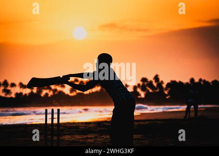 Junge spielt Cricket bei Sonnenuntergang am tropischen Strand in Sri Lanka Stockfoto