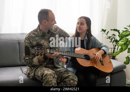 Der Veteran kam aus der Armee zurück. Ein Mann in Uniform mit seiner Tochter. Der Veteran spielt Gitarre. Stockfoto