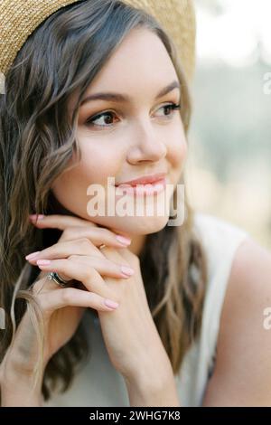 Lächelnde Frau in einem Strohhut mit den Händen unter ihrem Kinn Stockfoto