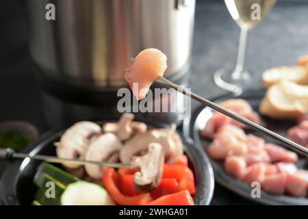 Stück rohes Fleisch auf einer langen Fonduegabel aufgespießt und etwas Gemüse, das in einem Topf mit heißem Öl frittiert wird, festliches Abendessen zum gemeinsamen Abendessen Stockfoto