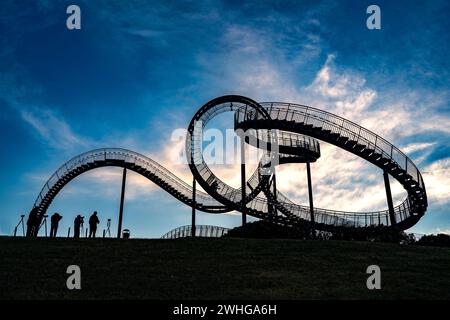 Fotografen mit Stativen als Silhouetten an der begehbaren Achterbahnskulptur Tiger and Turtle vor einem dunkelblauen Himmel mit Stockfoto