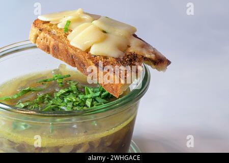 Zwiebelsuppe mit frischen grünen Kräutern im Glas und geröstetem Brot mit geschmolzenem Käse auf grauem Hintergrund, Kopierraum, s Stockfoto