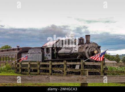 Amerikanische Flaggen winken im Wind, auf einem Zaun, während sich ein Dampfzug nähert Stockfoto