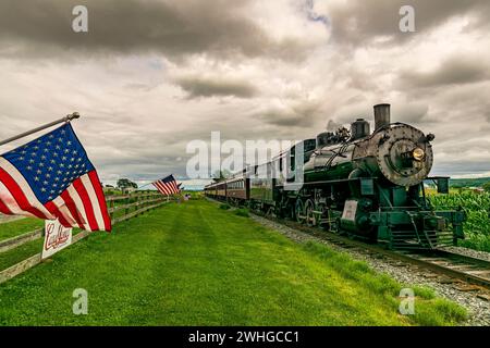 Amerikanische Flaggen winken im Wind, auf einem Zaun, während sich ein Dampfzug nähert Stockfoto