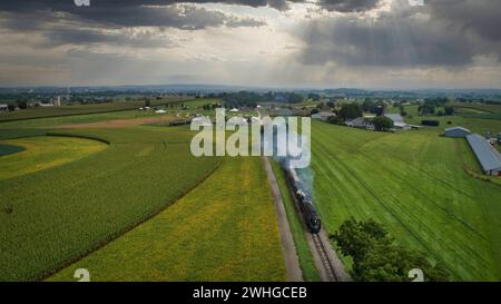 Drohnenansicht einer antiken Dampflok, Annäherung, Dampf blasen und Reisen auf dem Land Stockfoto