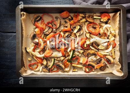 Backofen Gemüse wie Paprika, Tomate, Zucchini, Pilz, Fenchel und Auberginen auf einem Backblech auf dunklem rustikalem Holz, hoch angewinkelt Stockfoto