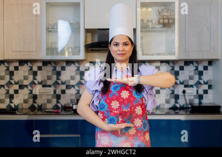 Schöne indianerin in Kochuniform mit Schürze, Kochmütze in der Küche, die mit Händen gestickt hat. Marketing- Und Werbekonzept. Stockfoto