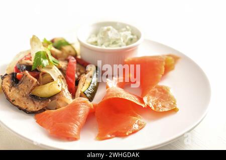 Geräucherter Lachs mit Gemüse und Dip auf einem weißen Teller, gesunder Snack mit niedrigen Kalorien für eine Schlankheitsdiät, ausgewählter Fokus Stockfoto