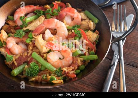 Meeresfrüchte-Gericht mit Garnelen, Reis, Hühnerfleisch und Gemüse in einer Paella-Pfanne auf einem dunklen rustikalen Holztisch, ausgewählte Fokus Stockfoto